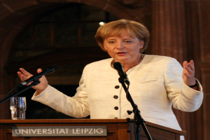 Bundeskanzlerin Angela Merkel hört eine Rede an einem Pult mit einem Mikrofon und einem Glas Wasser an der Universität Leipzig.