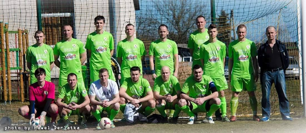 Gruppe von Männern in grünen T-Shirts stehend oder hockend auf einem Fußballfeld in der Nähe eines Torpfostens mit einem Fußball davor.