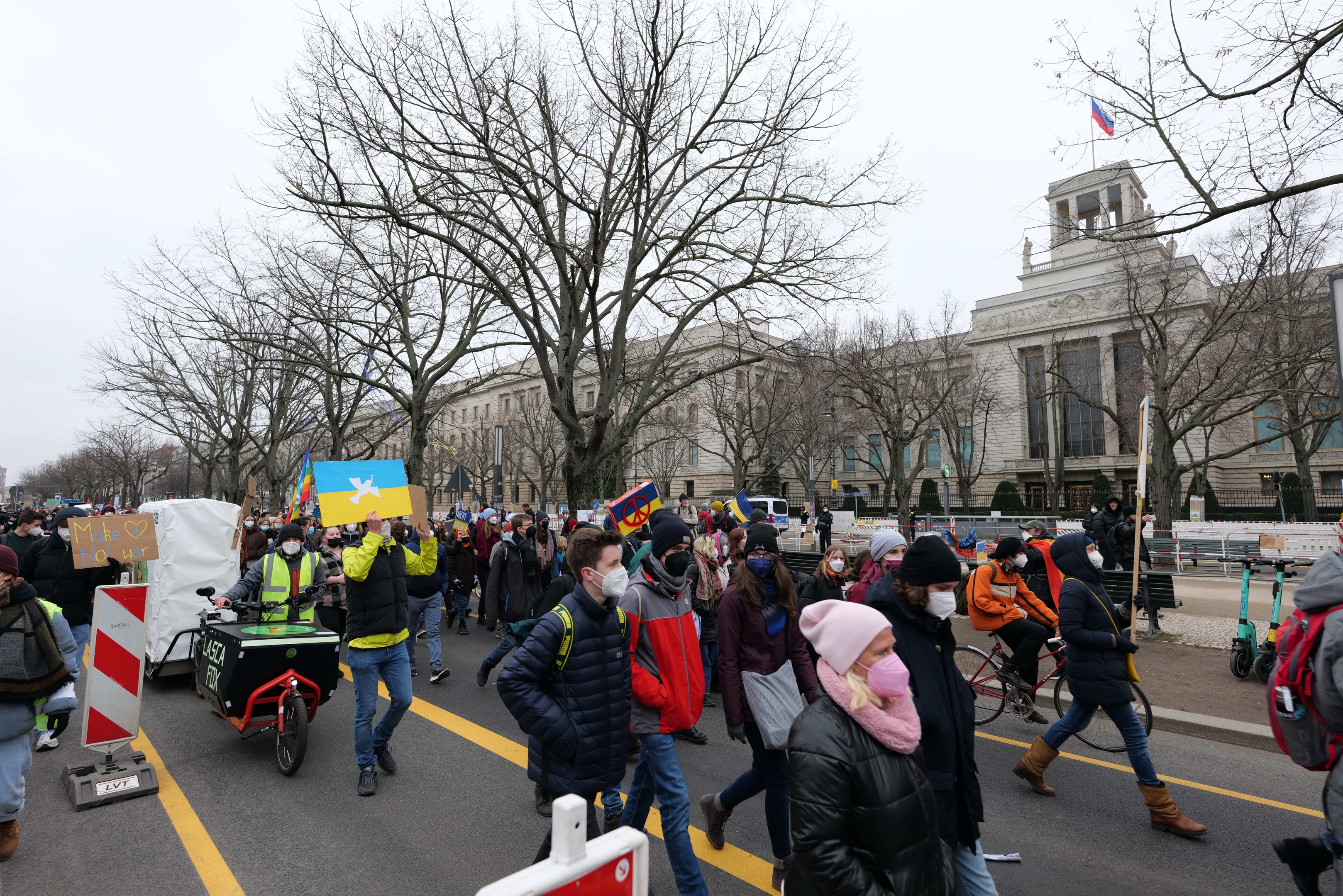 Eine große Gruppe von Menschen nimmt an einer Protestdemo in Washington, D.C. am 21. Januar 2020 teil und marschiert eine Straße entlang, mit Schildern, Bannern und Fahrrädern, vor einem Gebäude mit Bäumen und Schildern unter einem klaren blauen Himmel.
