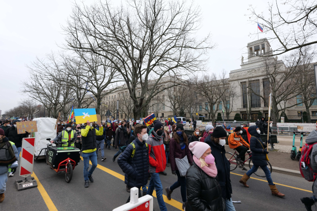 Eine große Gruppe von Menschen nimmt an einer Protestdemo in Washington, D.C. am 21. Januar 2020 teil und marschiert eine Straße entlang, mit Schildern, Bannern und Fahrrädern, vor einem Gebäude mit Bäumen und Schildern unter einem klaren blauen Himmel.