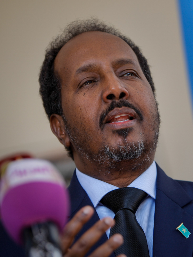 Ein Mann in Anzug und Krawatte, der in ein Mikrofon spricht und wahrscheinlich eine Zuschauermenge anspricht.