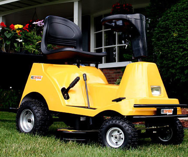 Ein gelber Rasenmäher vor einem Haus mit saftig grünem Rasen, Pflanzen, Blumen und Bäumen im Hintergrund.