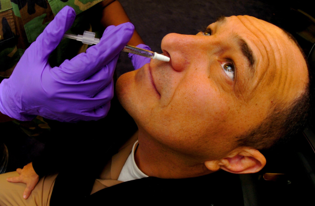 Ein Arzt in lila Handschuhen verimpft einem Mann eine Impfung durch Injektion in den Mund.