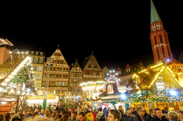 Ein geschäftiger Weihnachtsmarkt in Nürnberg, Deutschland mit Menschen um dekorierte Stände, Gebäuden mit Fenstern, einem Uhrenturm und einem dunklen Himmel.