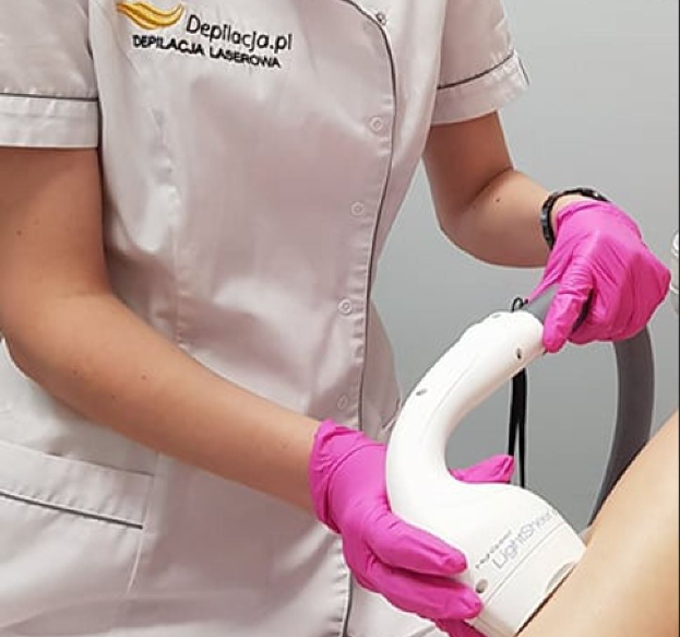 Eine Frau in einem weißen Hemd und pinken Handschuhen verwendet eine weiße Laser-Haarentfernungsmaschine auf ihrer Haut, während sie vor einer Wand steht.