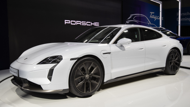 Weißer Porsche Taycan Turbo S E-Hybrid auf der IAA in Frankfurt, umgeben von schwarzen Schlafzimmermöbeln.