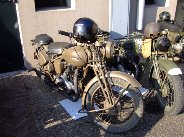 Zwei Motorräder nebeneinander vor einem Gebäude mit Fenstern, einer Tür und einem Rohr an der Seite geparkt, mit Helmen auf dem Boden.