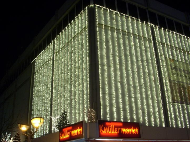 Ein Gebäude in Berlin, Deutschland, geschmückt mit Weihnachtslichtern, umgeben von Bäumen, Laternenmasten und Texttafeln, mit dem Himmel im Hintergrund.