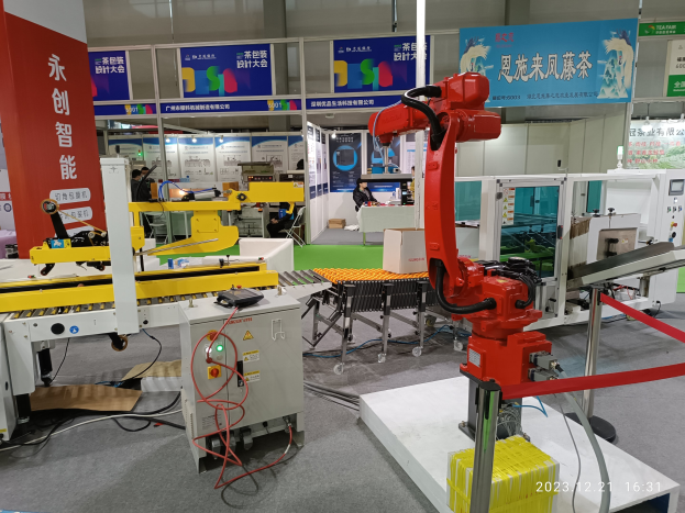 Gruppe von Robotern auf einem Tisch in einer Fabrikumgebung umgeben von Maschinen, Kabeln, Text-bedruckten Platinen und Beleuchtung, mit Menschen im Hintergrund.