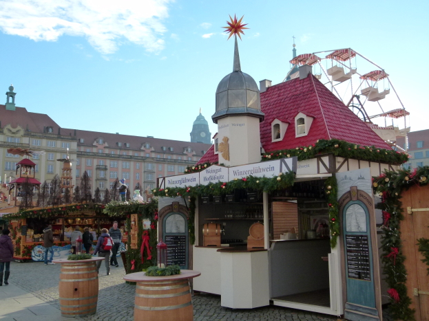 Ein geschäftiger Weihnachtsmarkt in Nürnberg, Deutschland, mit Menschen um geschmückte Stände, festliche Lichter, ein Riesenrad, Gebäude und ein Schild auf der rechten Seite.
