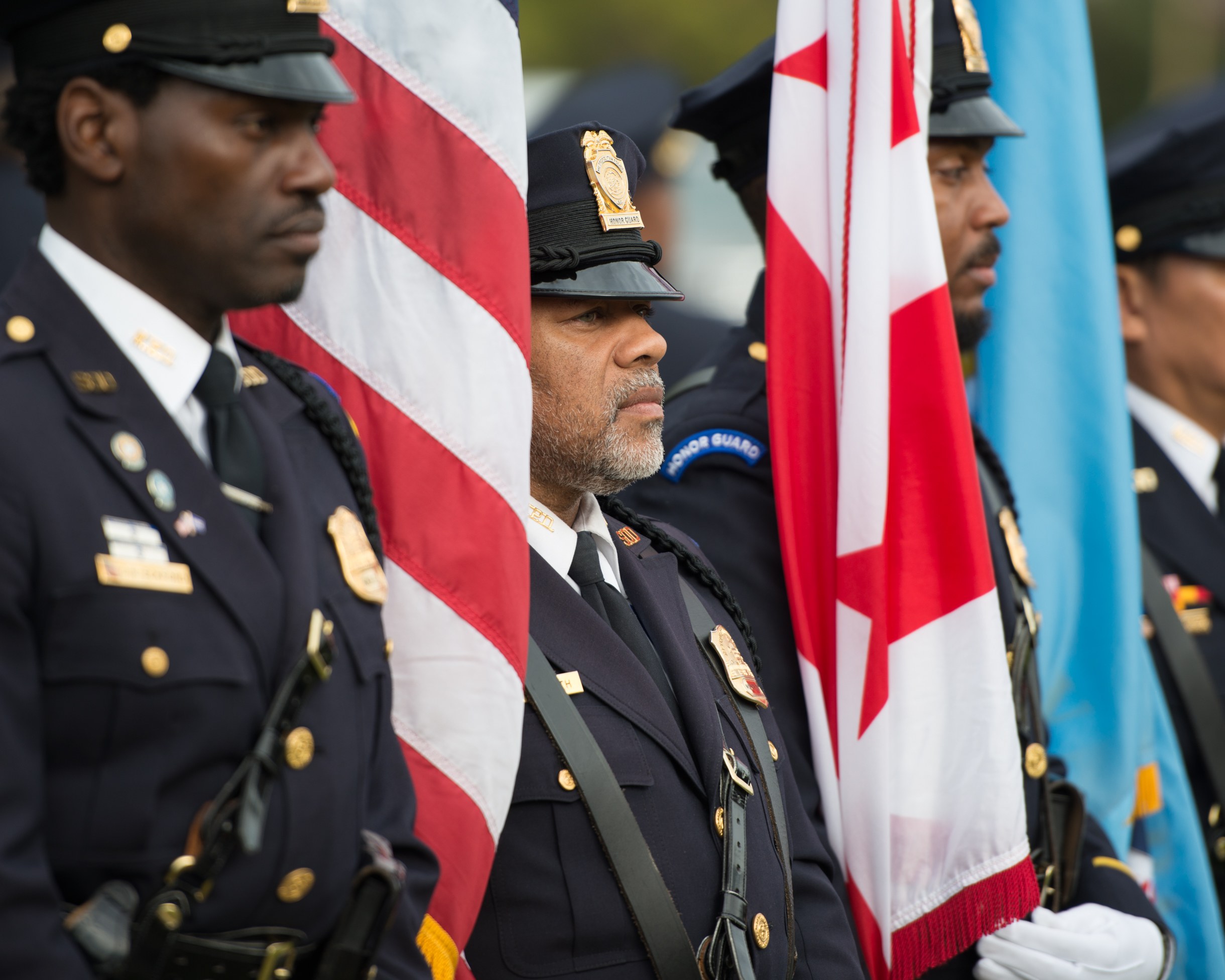 Gruppe von Polizisten in Uniform, die zusammenstehen und Fahnen halten, vor einem unscharfen Hintergrund.