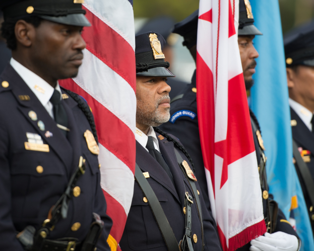Gruppe von Polizisten in Uniform, die zusammenstehen und Fahnen halten, vor einem unscharfen Hintergrund.