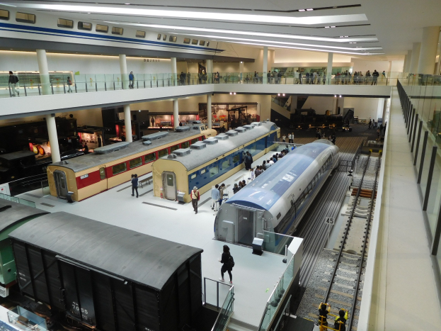 Großer Museumsraum mit verschiedenen Bahnen in unterschiedlichen Größen und Farben, mit Menschen, die beobachten, und Geländern, Säulen und Deckenleuchten.