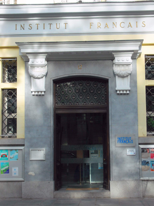 Der Eingang des Institut Français in Paris, mit einem Gebäude mit Fenstern, einer Tür und Plakaten an der Wand, und einer Straße unten.