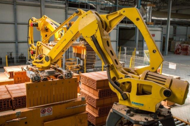 Großes industrielles Lager mit gestapelten Kisten, Überdachkränen, Zaun, Pfosten und einer fernen Wand in einer automatisierten Manufacturing-Umgebung.