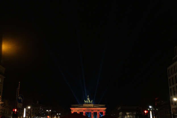 Brandenburger Tor in Berlin nachts, beleuchtet von Straßenlaternen, mit umliegenden Gebäuden, Bäumen, Pfählen, Verkehrszeichen, Schildern und Zelten gegen einen dunklen Himmel.