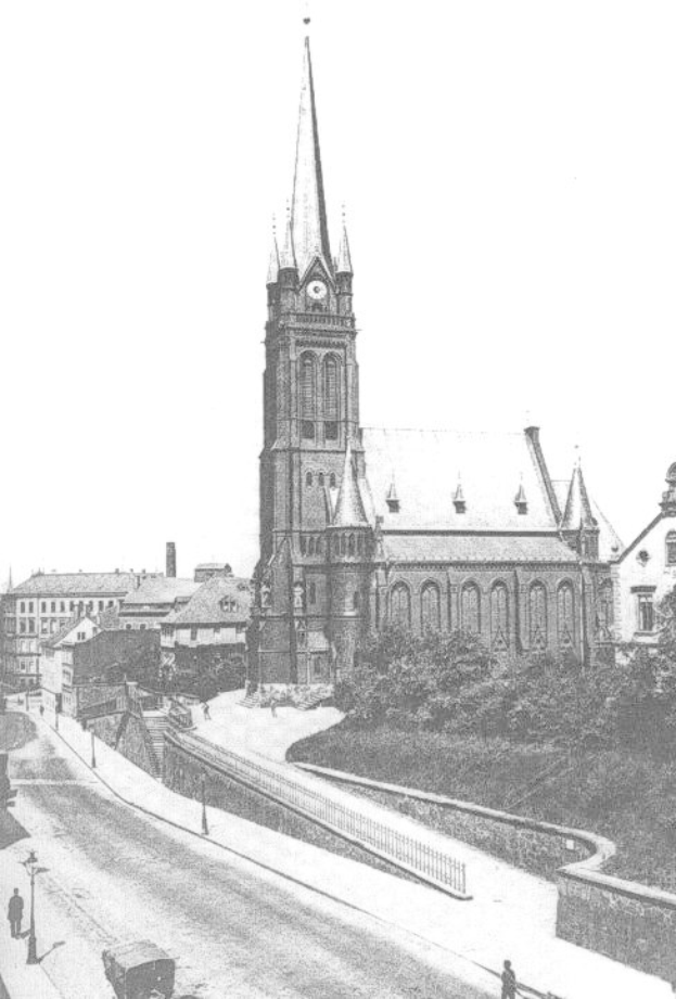 Schwarz-weiß-Foto einer Stadtstraße mit St. Peter Kirche im Hintergrund, gesäumt von Gebäuden, Bäumen, Fahrzeugen und einigen Passanten.