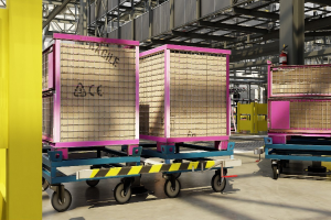 Großes Lager mit gestapelten Kisten auf Wagen, einer gelben Säule links und einem Feuerlöscher rechts, mit Metallstangen und anderen Gegenständen im Hintergrund.