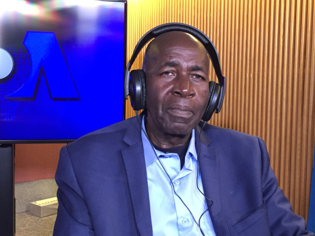 Ein Mann in Anzug und Kopfhörern sitzt vor einem Fernseher und spricht während einer Diskussion über das Verbot des Internets in Nigeria, mit einer hölzernen Wand im Hintergrund.