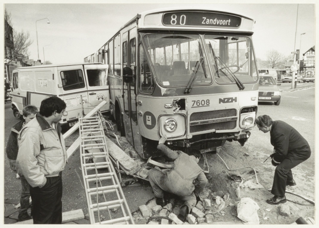 Schwarzes und weißes Foto eines auf der Straße liegenden Busses mit Menschen und Werkzeugen in der Nähe, umgeben von Gebäuden, Bäumen, Masten und Himmel.
