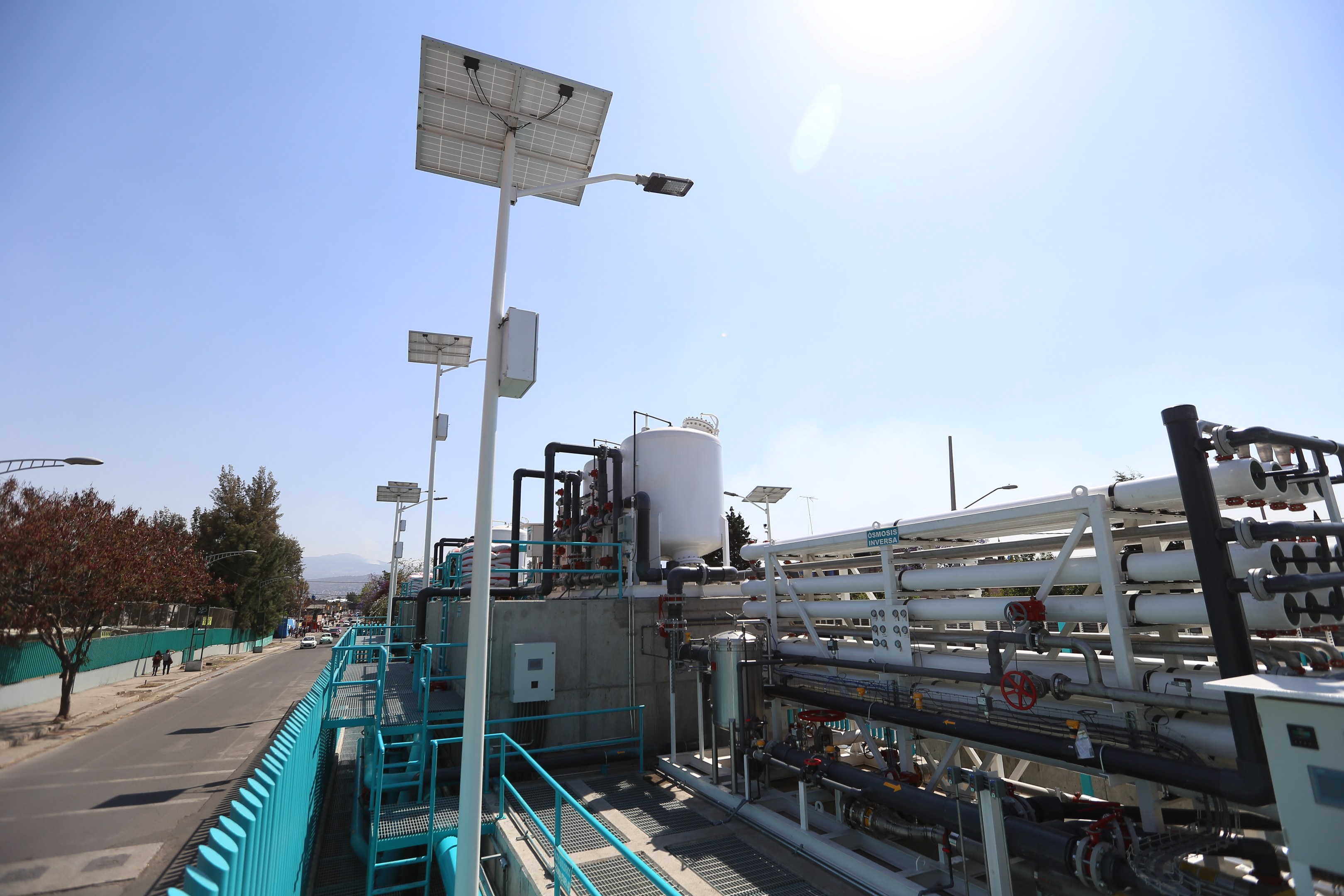 Großes industrielles Gebäude mit umfangreichen Rohrleitungen, Solarpanelen, Geländern und Infrastruktur, vor einem Hügel- und klaren Himmel, Teil einer Wasseraufbereitungsanlage in Kalifornien.