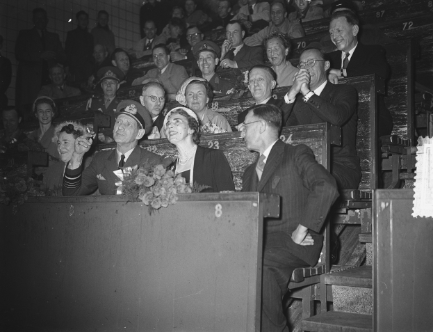 Schwarzes und weißes Foto einer Menschenmenge in einem Stadion mit Sitzplätzen und Stehplätzen, einem Podium mit Blumenstrauß, Treppen auf der rechten Seite und einer Wand im Hintergrund.
