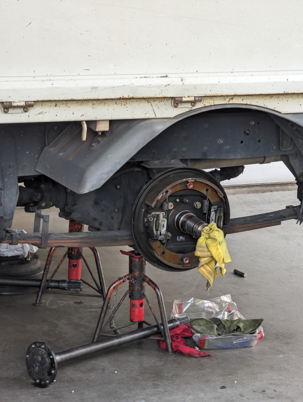 Ein gelbes Tuch liegt über einem Lastwagen, der in einer Garage geparkt ist, mit Werkzeugen und Gegenständen, die vor ihm auf dem Boden verstreut sind.