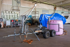 Ein blauer Planen-Trailer, der an einem Fahrzeug in einer Garage befestigt ist, mit verstreuten Gegenständen auf dem Boden und beleuchteten Wänden im Hintergrund.