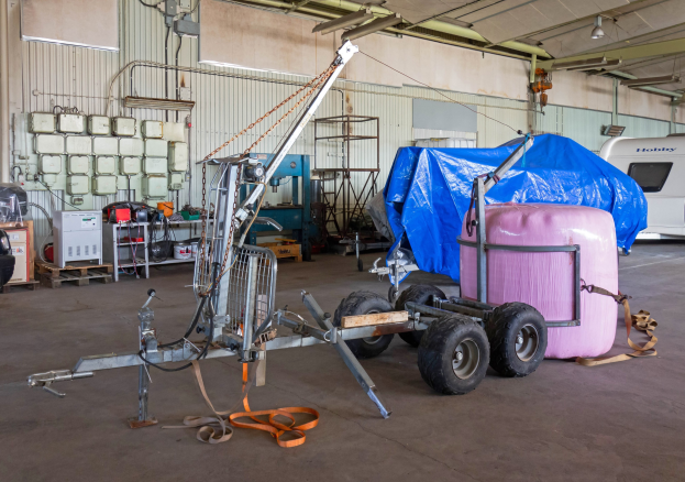 Ein blauer Planen-Trailer, der an einem Fahrzeug in einer Garage befestigt ist, mit verstreuten Gegenständen auf dem Boden und beleuchteten Wänden im Hintergrund.