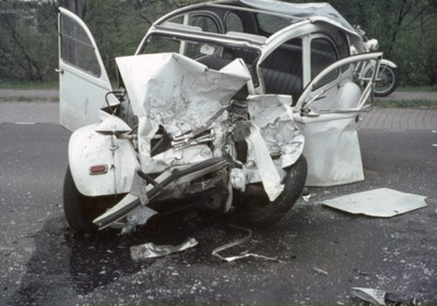 Schwerbeschädigte Autos am Straßenrand mit Frontalaufprall, umgeben von Bäumen und einem entfernten Gebäude.