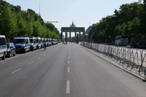 Eine lange Reihe von Polizeiwagen, die auf der Straße vor dem Brandenburg-Tor in Berlin, Deutschland, geparkt sind, mit Fahrradfahrern und Fußgängern in der Nähe, Absperrungen, Bäumen und einem Bogen mit Statuen im Hintergrund.