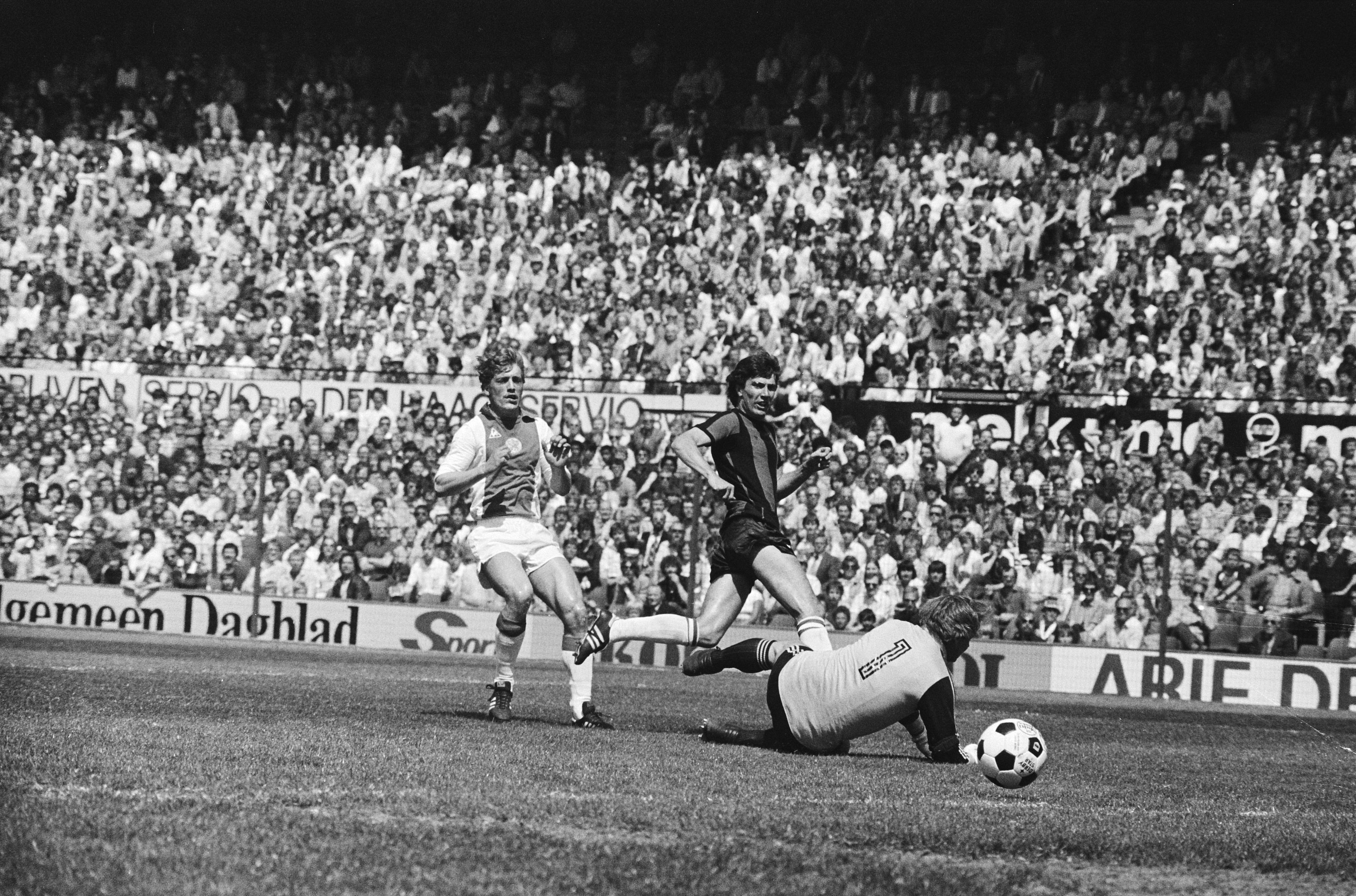 Schwarz-weißes Foto von Fußballspielern im Einsatz auf einem Feld mit Zuschauern im Hintergrund und einer "Bundesliga 1978-79 Ajax 1-1 Hannover 96"-Tafel.