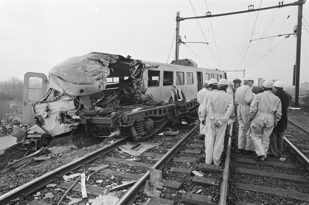Ein Schwarz-Weiß-Bild einer Zugkollision auf den Schienen mit Einsatzkräften in Helmen und sichtbarem Umfeld.