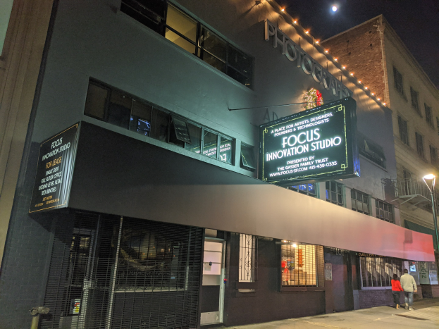 Außensicht des Focus Innovation Studios in New York City bei Nacht, mit beleuchteten Gebäuden, Passanten auf dem Gehweg und sichtbarem Himmel.