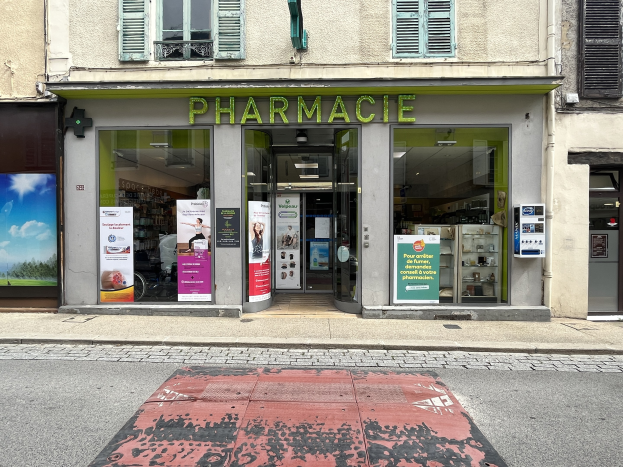 Apotheke mit Glaswänden und -türen, Plakate an den Wänden, befindet sich an der Ecke einer Straße mit einer Straße unten.