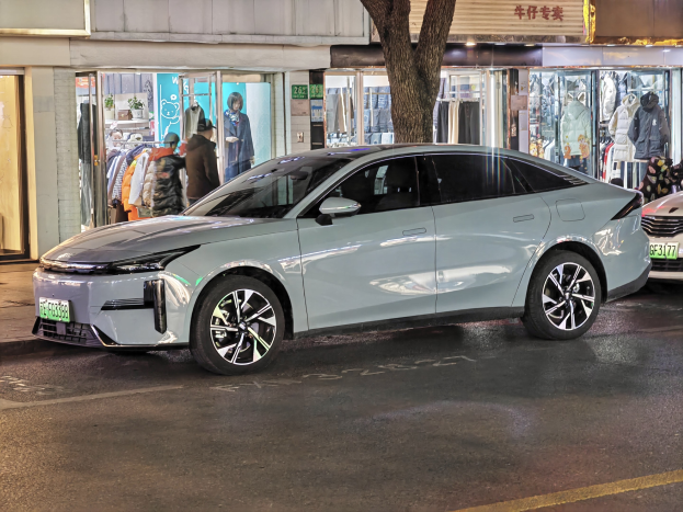 Elektrischer Mitsubishi Lancer EV auf einer nächtlichen Stadtstraße geparkt, umgeben von Gebäuden, beleuchteten Schaufenstern, Schaufensterpuppen und Schildern.