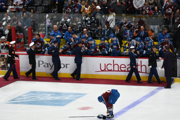 Eishockeyspieler auf dem Eis umgeben von Menschen mit Mützen und Eishockeyschläger, mit Zuschauern im Hintergrund und Tafeln mit "Colorado Avalanche vs San Jose Sharks - 3/24/15 NHL Pick, Odds, and Prediction".