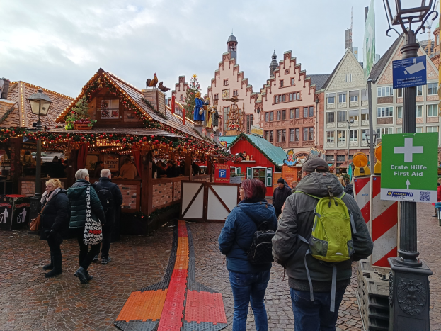Menschen, die auf einem Kopfsteinpflasterweg neben einem Weihnachtsmarkt in Nürnberg, Deutschland, gehen, mit Laternenmasten und Texttafeln im Blickfeld, Gebäuden und bewölktem Himmel im Hintergrund.