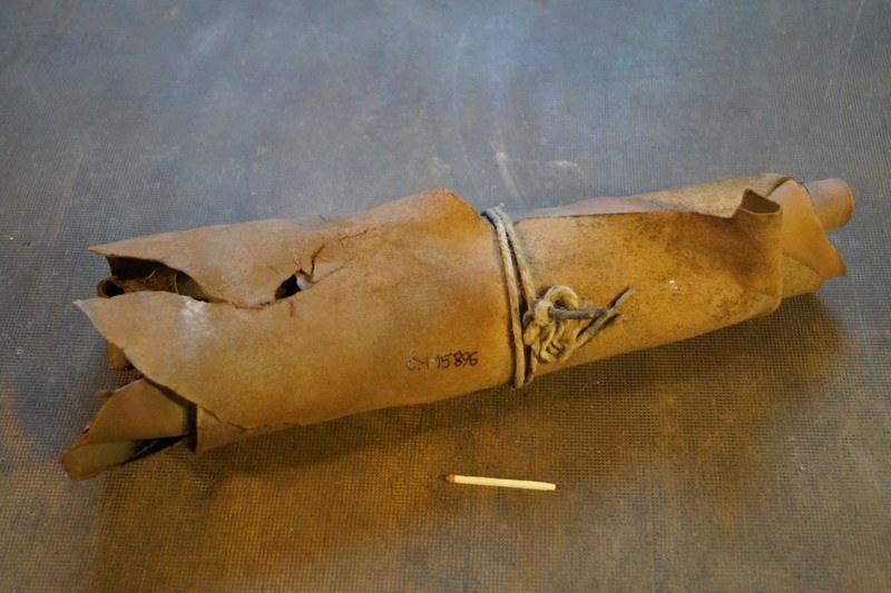 Ein brauner Papiertüte in Form einer Granate, mit einem Seil zugeschnürt, liegt auf einem Tisch mit einer Zigarette daneben.