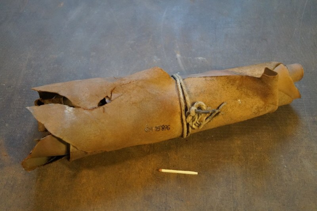 Ein brauner Papiertüte in Form einer Granate, mit einem Seil zugeschnürt, liegt auf einem Tisch mit einer Zigarette daneben.