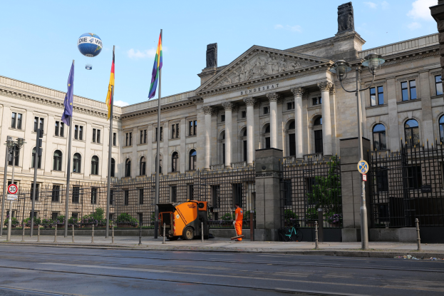 Großer moderner Bau mit zahlreichen Fenstern, identifiziert als der Bundestag in Berlin, Deutschland, umgeben von Straßeninfrastruktur, Passanten und Bäumen unter einem bewölktem Himmel.