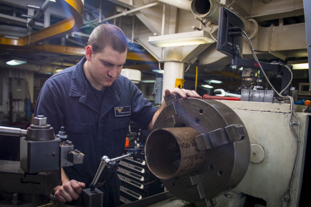 Ein Fräser, der industrielle Maschinen in einer Fabrikumgebung bedient, umgeben von Beleuchtung, Rohren und Equipment.
