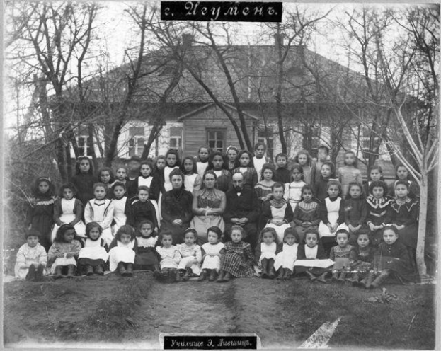 Schwarz-weiß-Foto von Kindern, die vor einem Fensterbau mit Text 'Jugoslawien, die erste Schule der Welt' posieren.