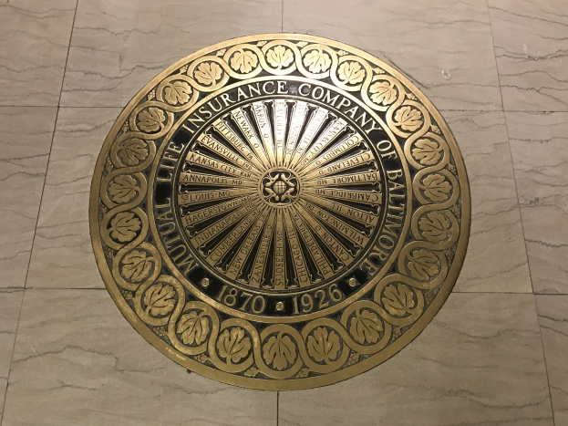 Runder goldener Schild auf dem Boden eines Gebäudes mit der Inschrift "Gebäudeversicherungsgesellschaft Baltimore".