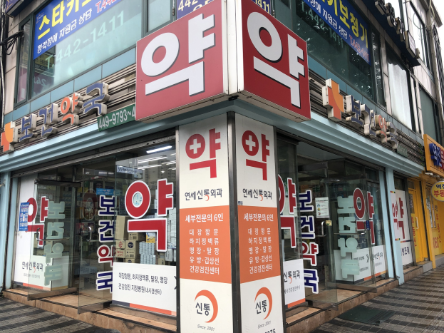Außenansicht einer modernen Glaswand-Apotheke in Seoul, Südkorea, mit einem Schild und Informationsschildern, die darauf hinweisen, dass es sich um die erste Apotheke in Südkorea handelt.