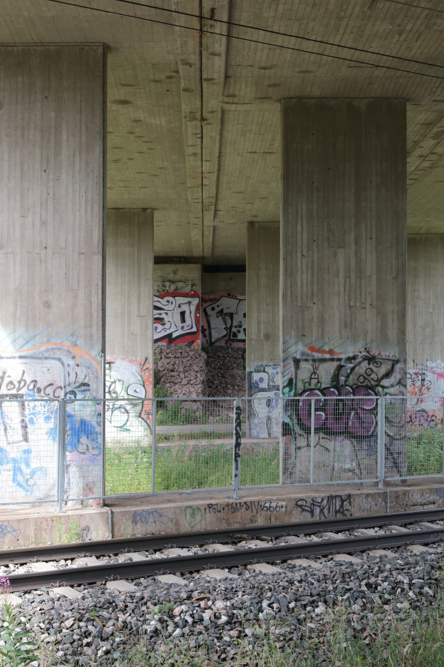 Eisenbahnschiene mit Graffiti an der Seite, von Steinen, Gras, einem Zaun, Säulen, Drähten und einem Dach umgeben