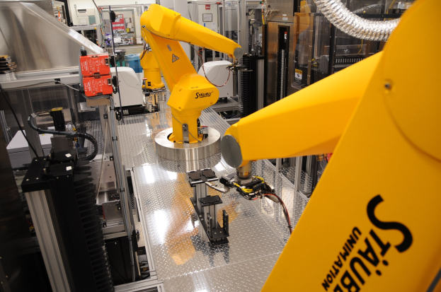 Ein gelber Roboter bedient Maschinen in einer industriellen Fabrikumgebung mit sichtbaren Rohren und beleuchteten Wänden.