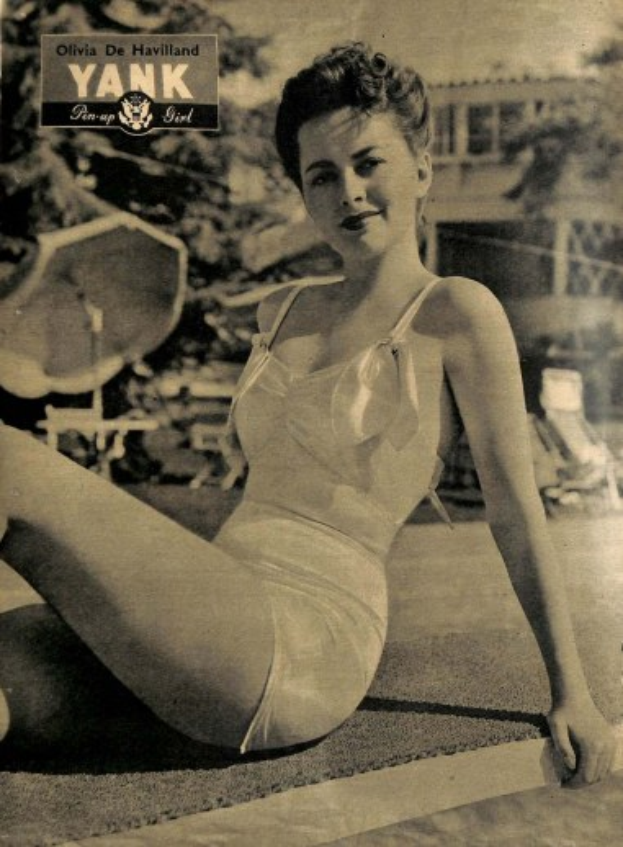 Olivia de Havilland in einem Badeanzug auf dem Boden sitzend und lachend, mit Bäumen, Stühlen, einem Gebäude und Text im Hintergrund.