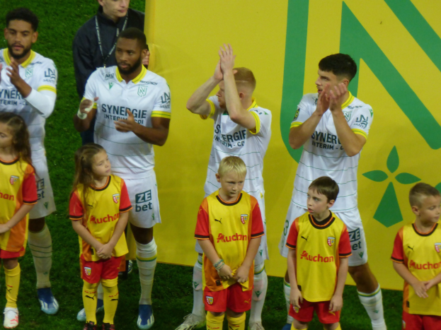 Eine Gruppe von Fußballspielern in Uniform klatscht auf einem Ligue 1-Feld in Feierlaune, mit einem "Ligue 1"-Schild im Hintergrund.