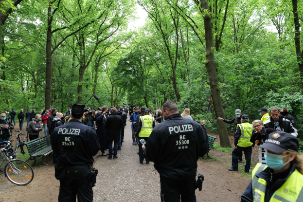 Polizisten vor einer Menge bei einer Outdoor-Veranstaltung mit Fahrrädern und einer Bank im Vordergrund